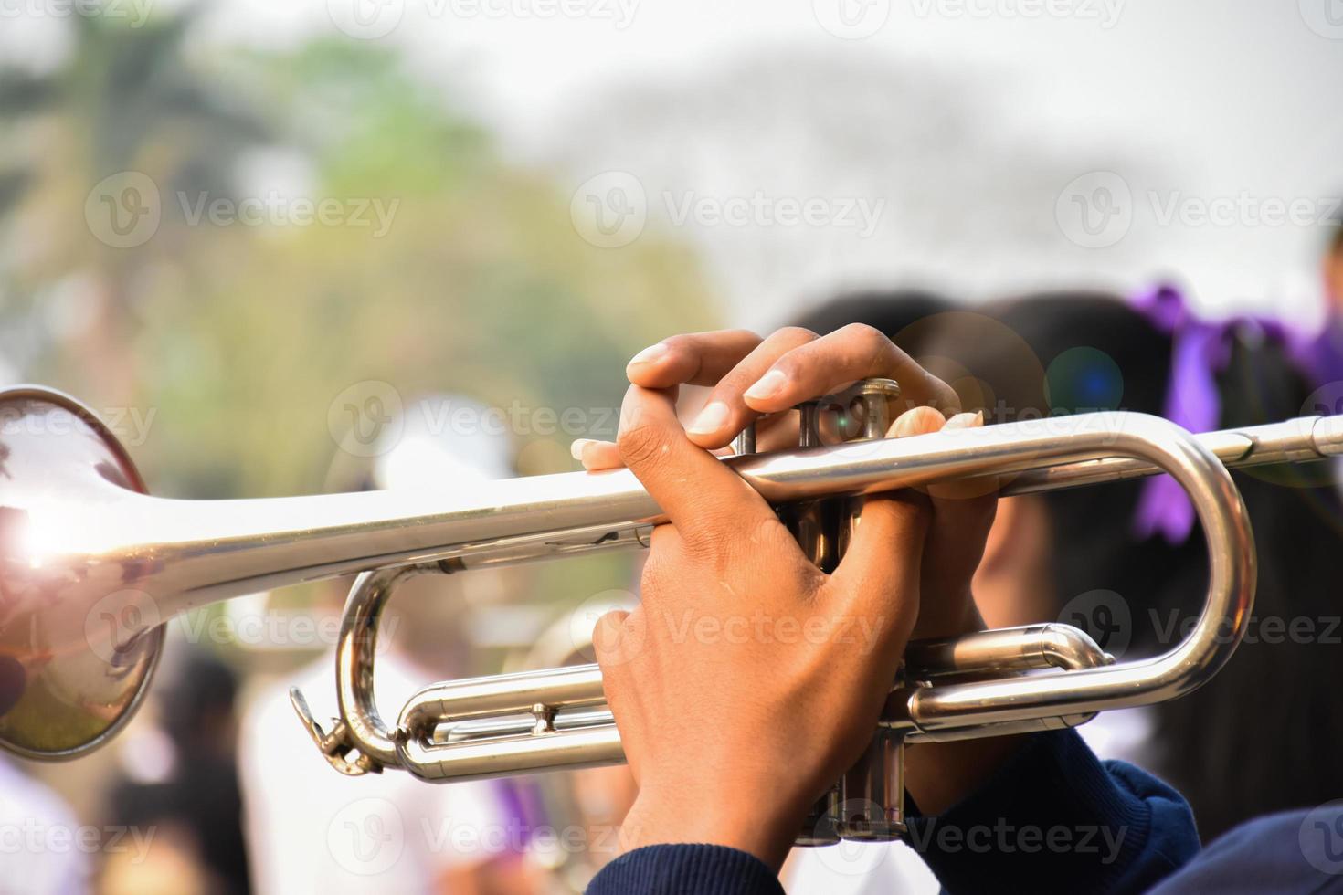 estudiante asiático joven que sopla una trompeta con la banda de música de la escuela, fondo borroso foto