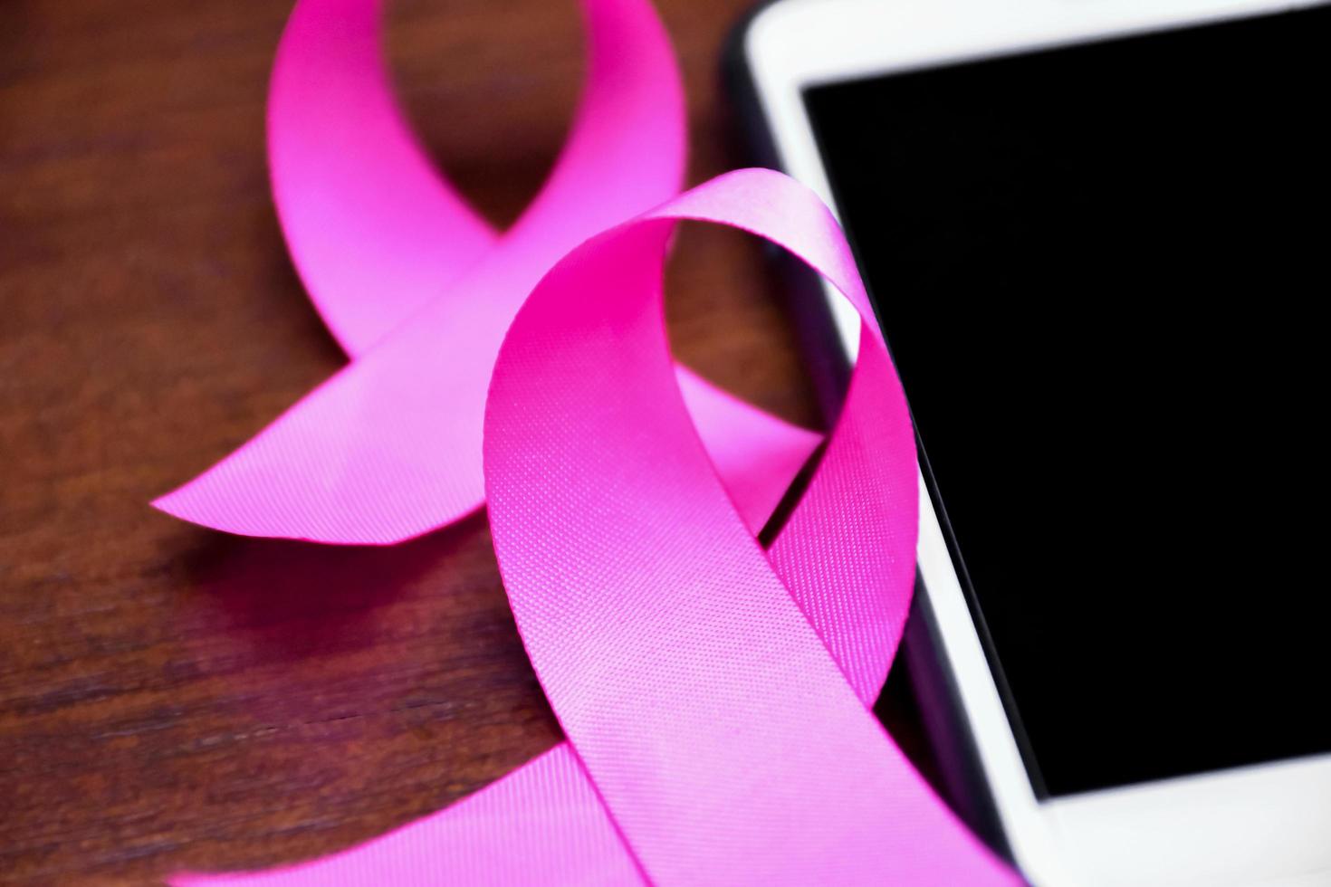 Pink ribbon on table with mobile phone. Concept for protesting and supporting the breast cancer against in woman. photo