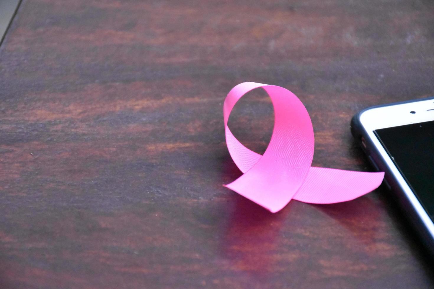 Pink ribbon on table with mobile phone. Concept for protesting and supporting the breast cancer against in woman. photo