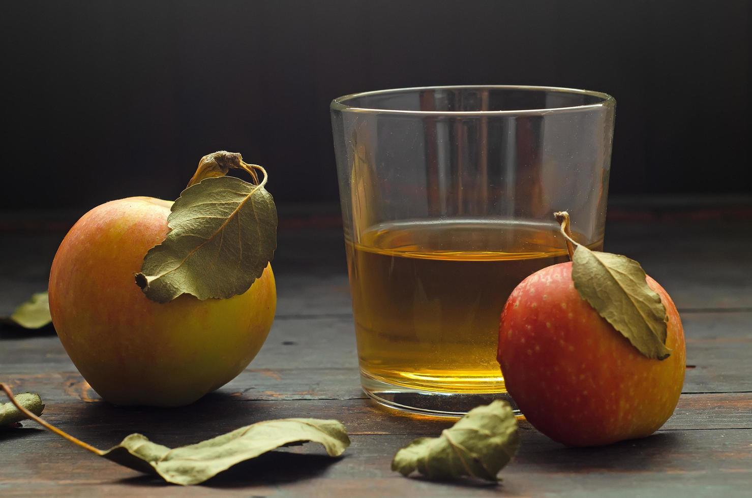 un vaso con vinagre de sidra de manzana y dos manzanas con hojas sobre fondo de madera. foto