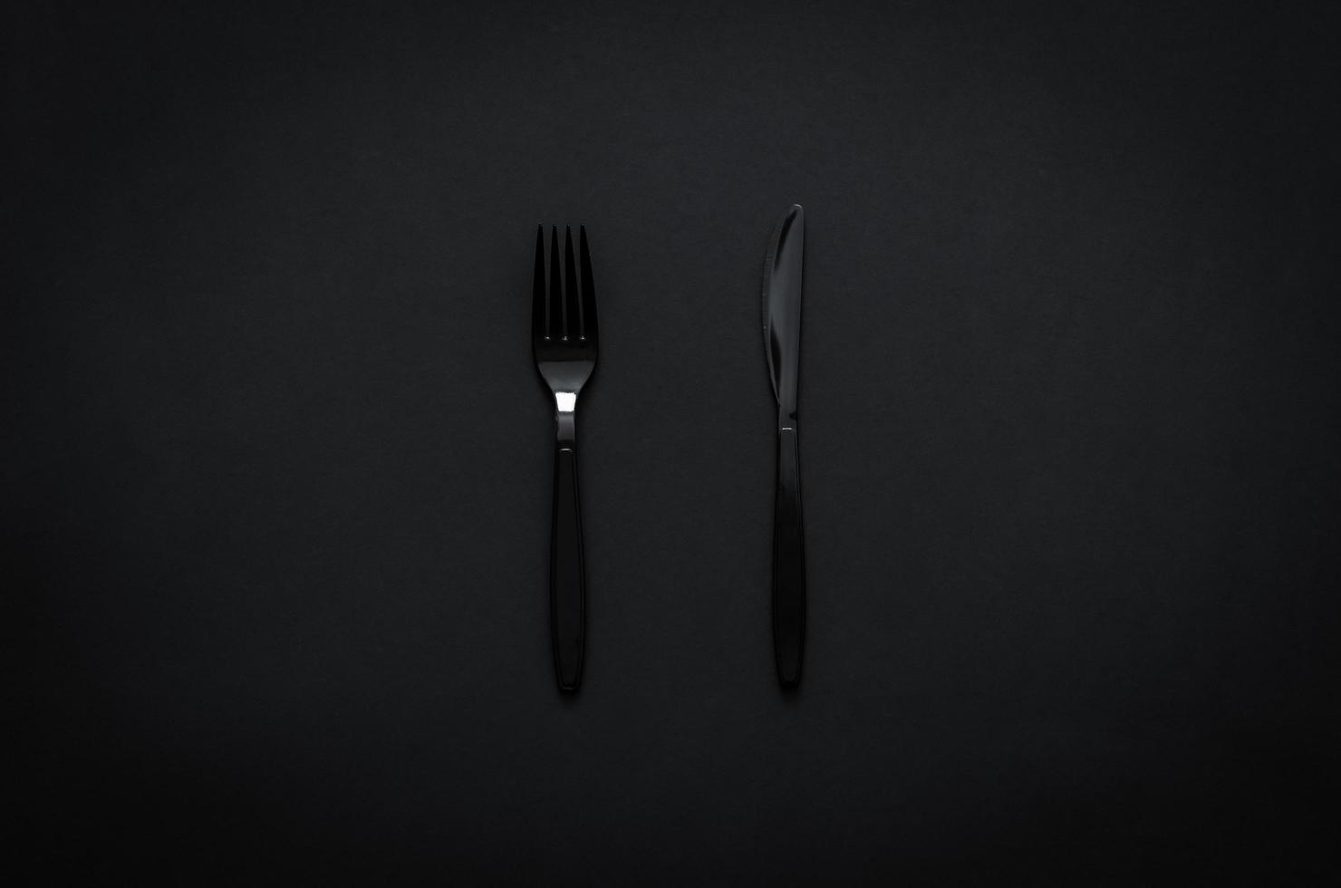Fork and knife on dark background for minimalist flat lay black food concept. photo