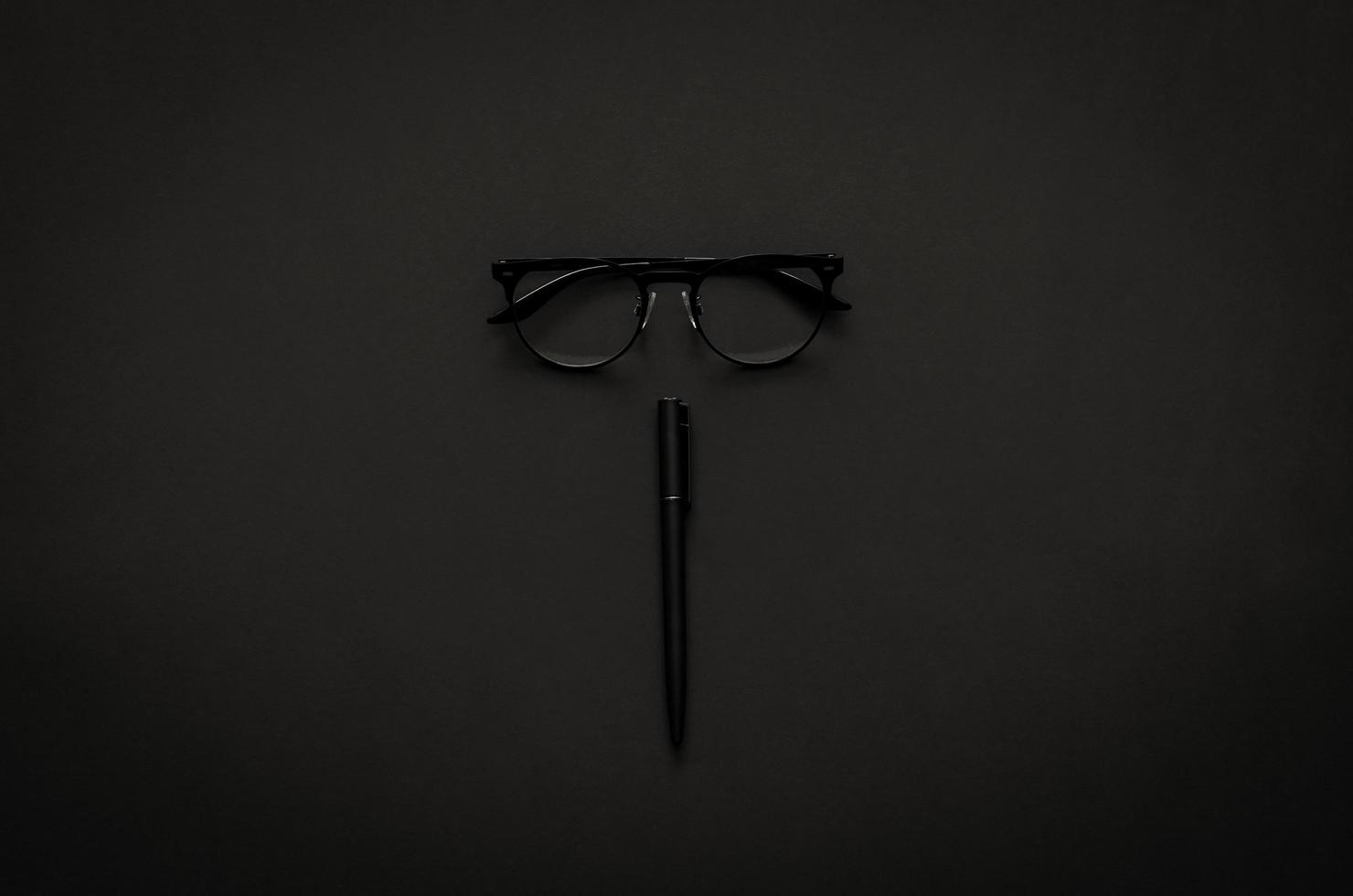 Eyeglasses and pen in modern lifestyle on dark background for minimalist flat lay black concept. photo