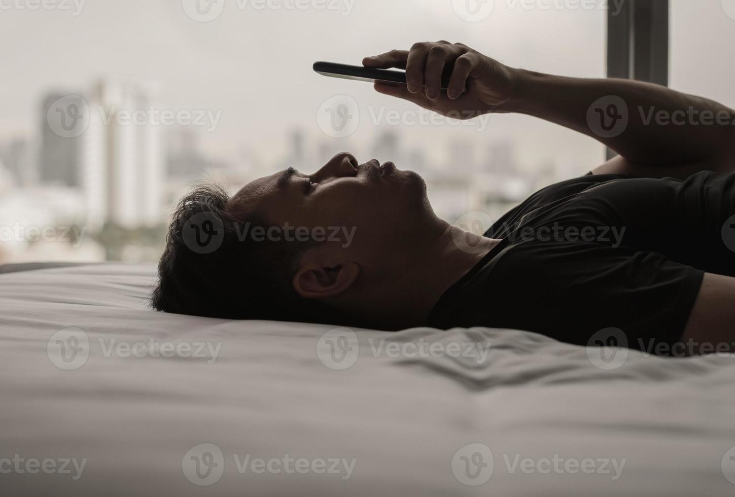 Asian man feels sad on bed looking and focus on smartphone. Internet social media addiction and mental health concept. photo