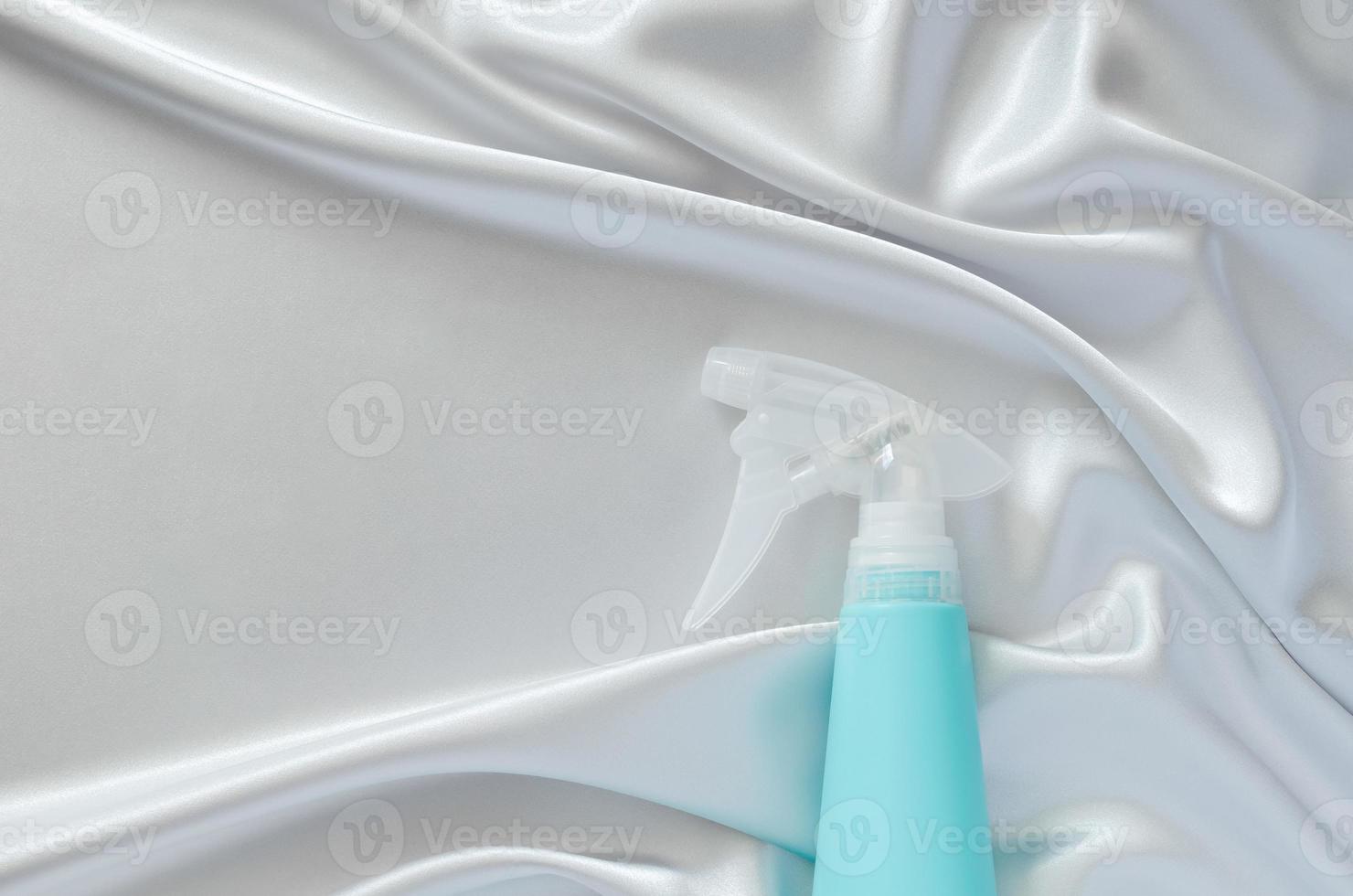 Water spray bottle on smooth and wavy grey cloth texture with space for text. Housekeeping concept. photo