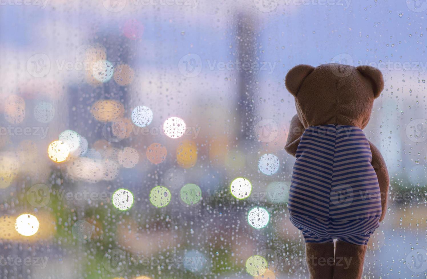 Teddy bear crying alone at window when raining with colorful bokeh lights. photo