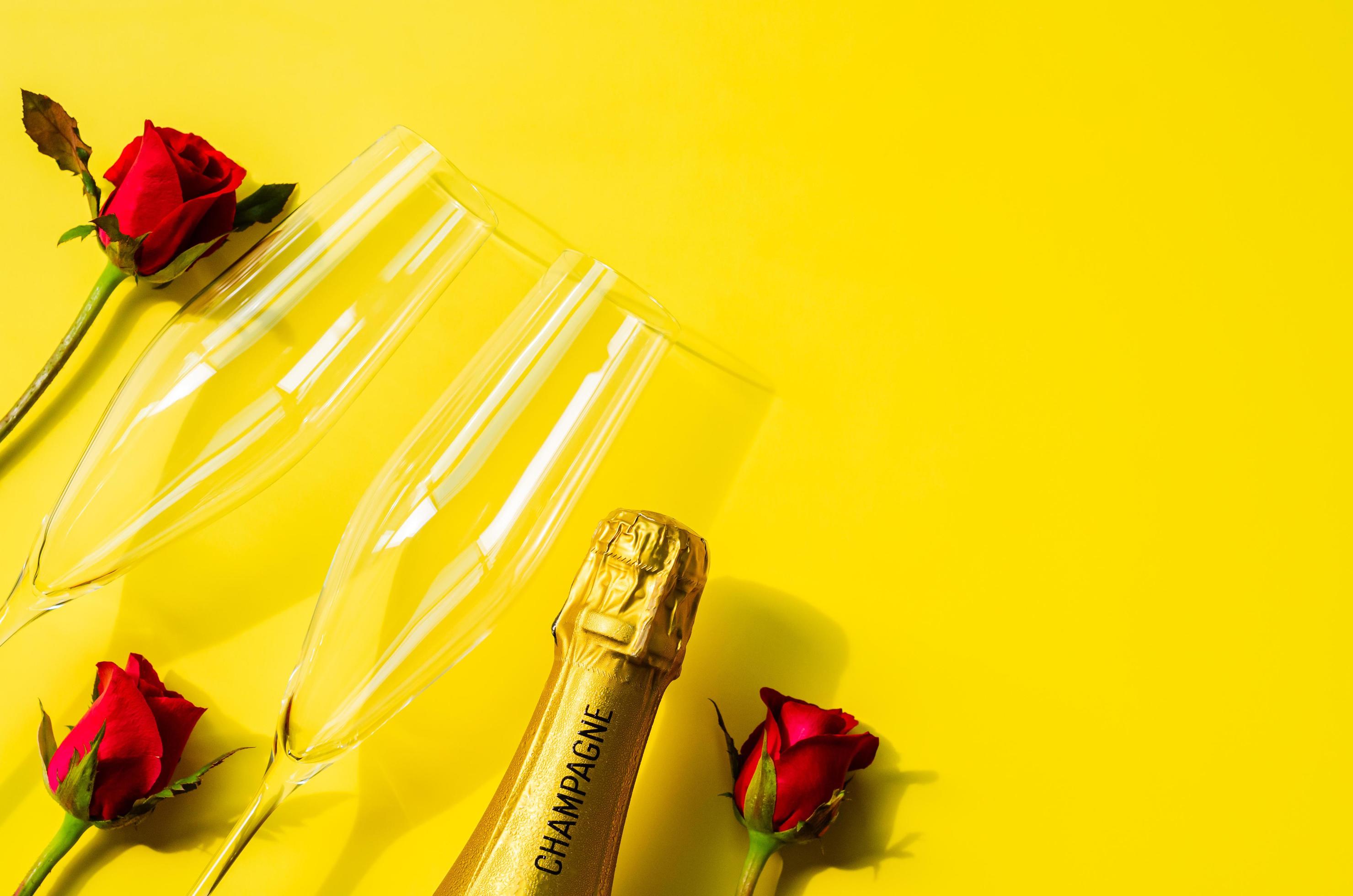 Champagne bottle with two glasses and rose flowers on yellow background