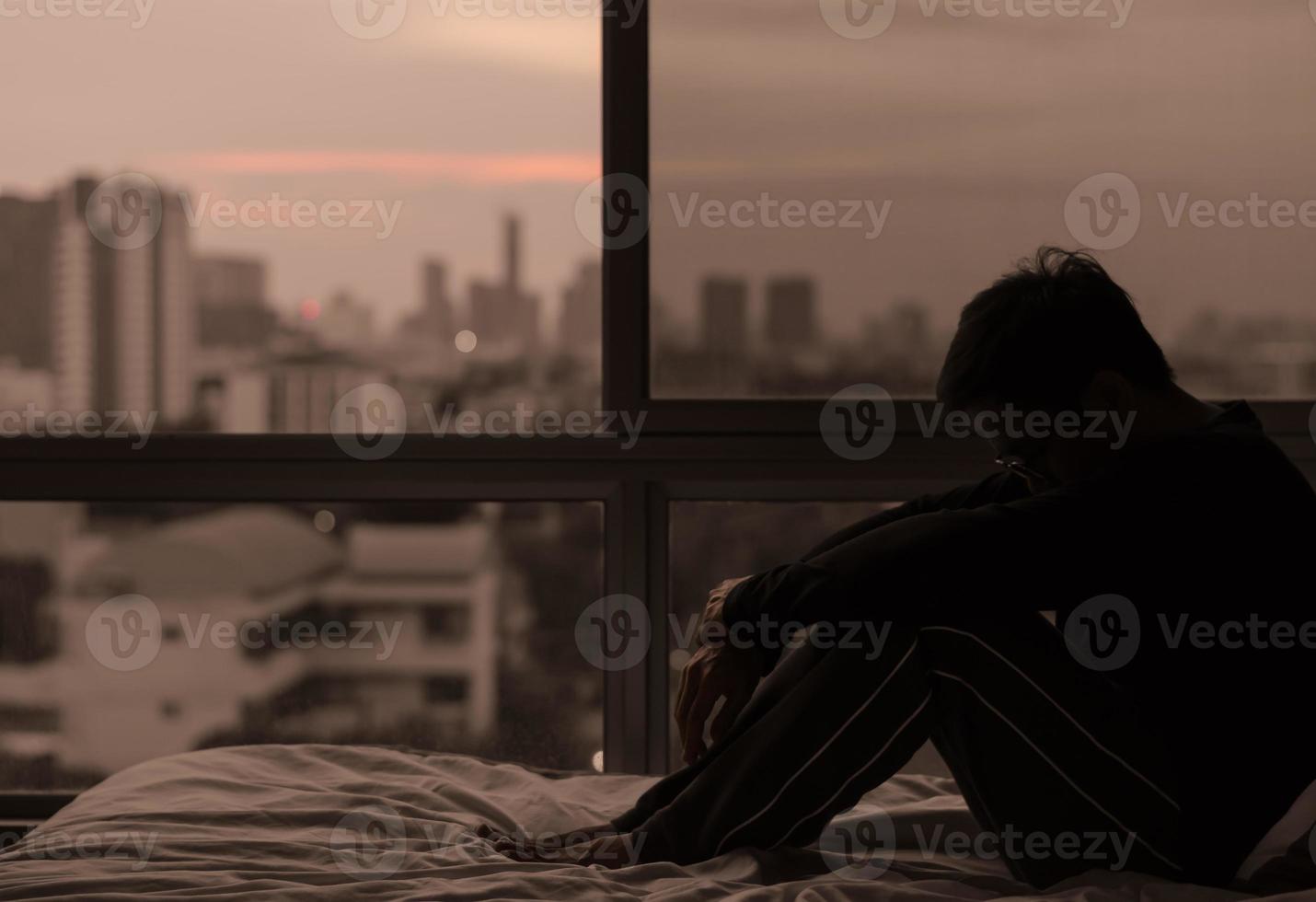 The man sitting on bed with city view from bedroom. photo