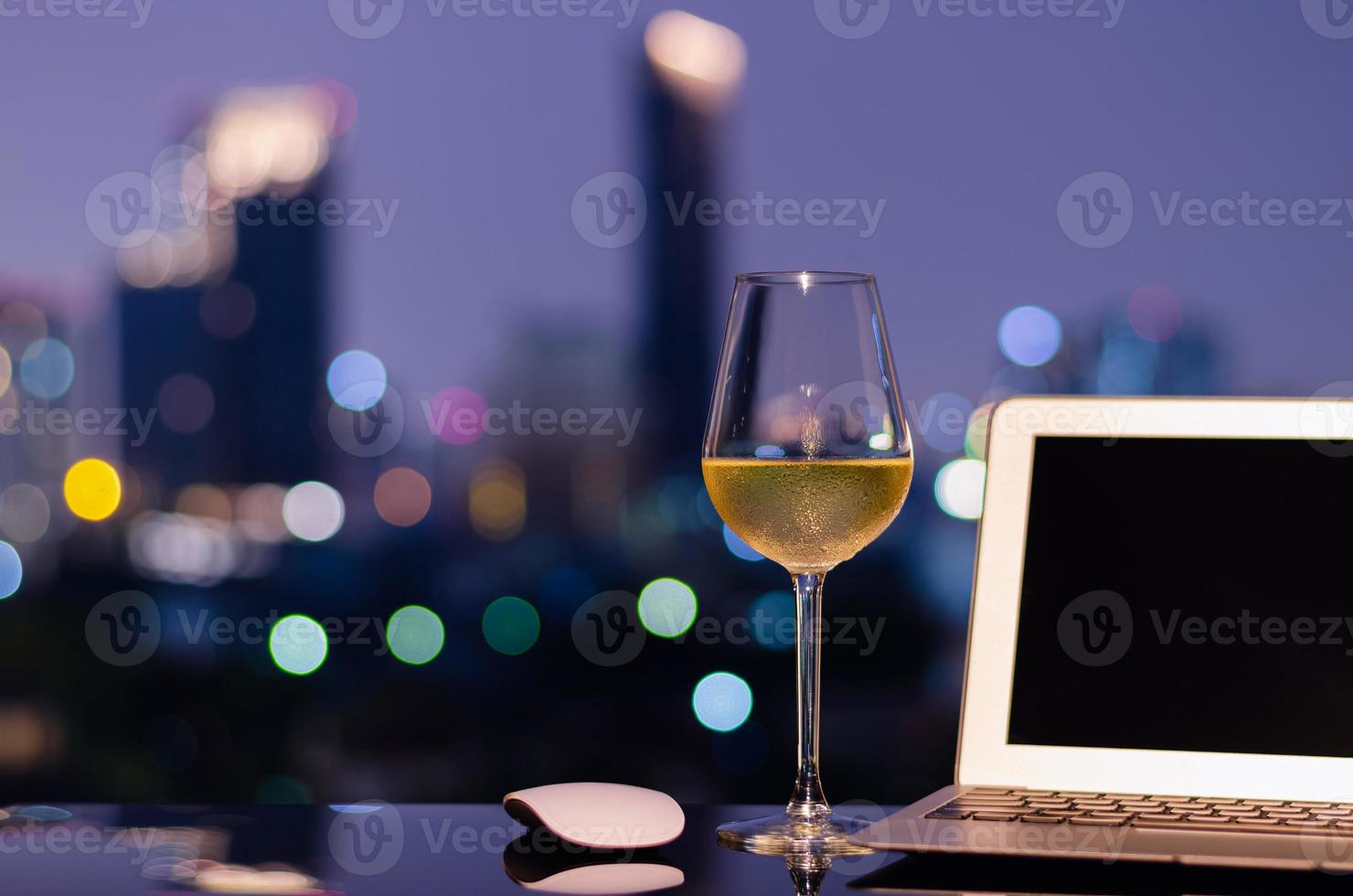 A glass with white wine puts on table with laptop computer and colorful city bokeh lights. Working from home concept. photo