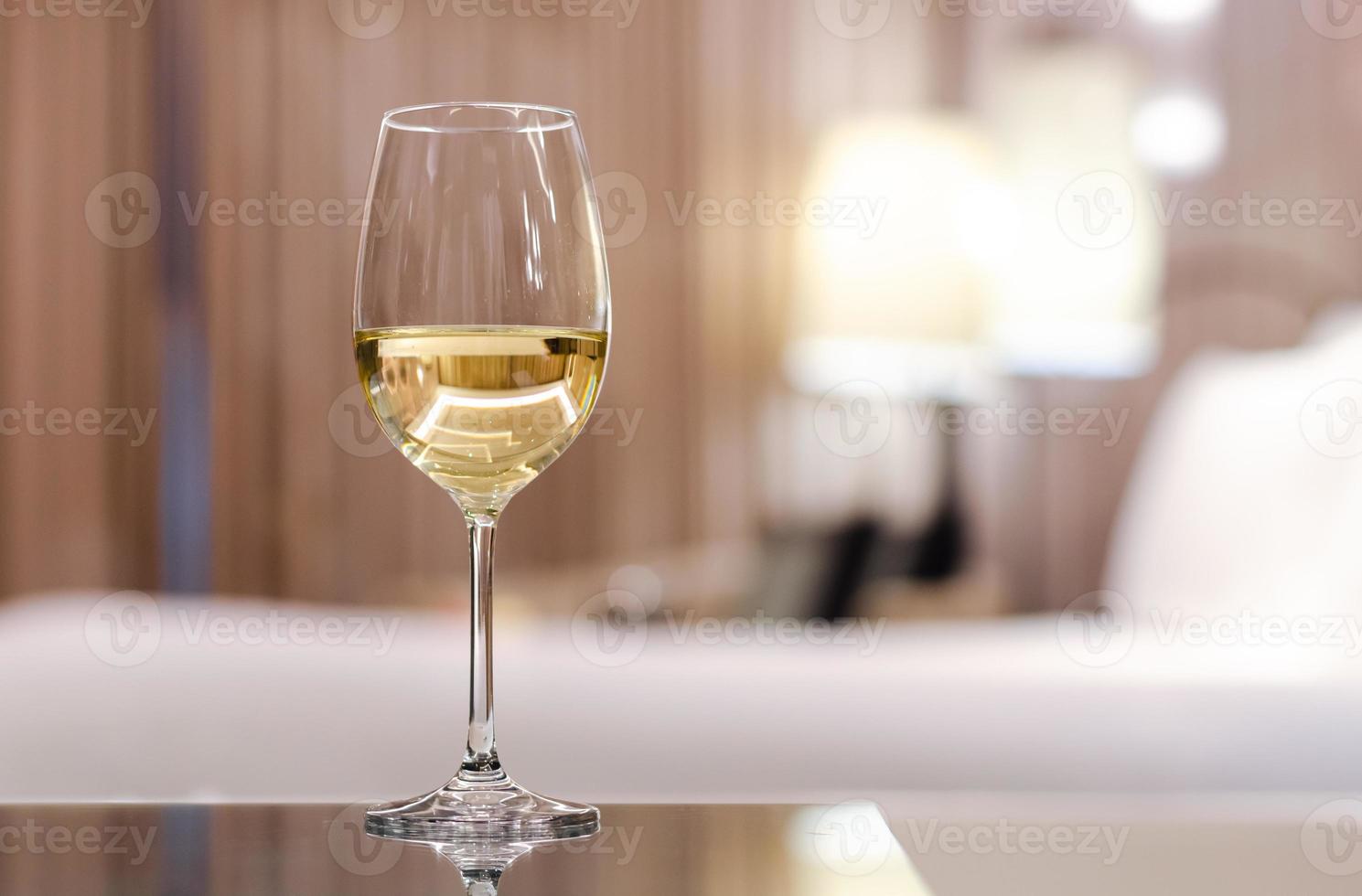 A glass of white wine puts on table in bed room. Relaxing at home concept. photo