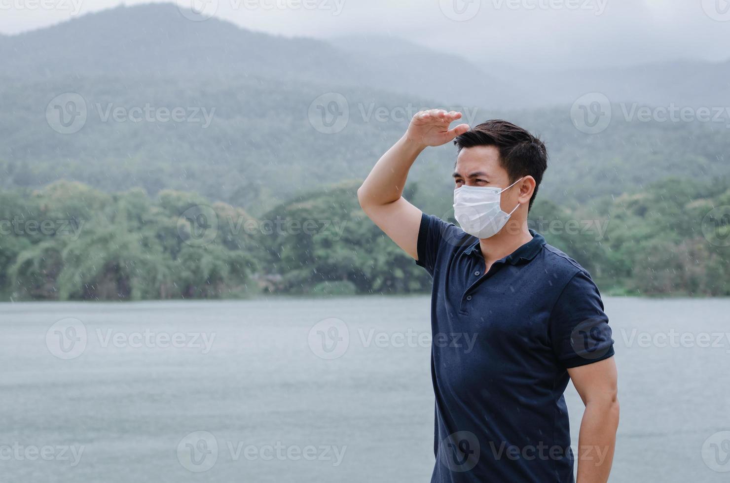 hombre asiático con mascarilla para protegerse de enfermarse y mojarse de la lluvia en la temporada del monzón. foto