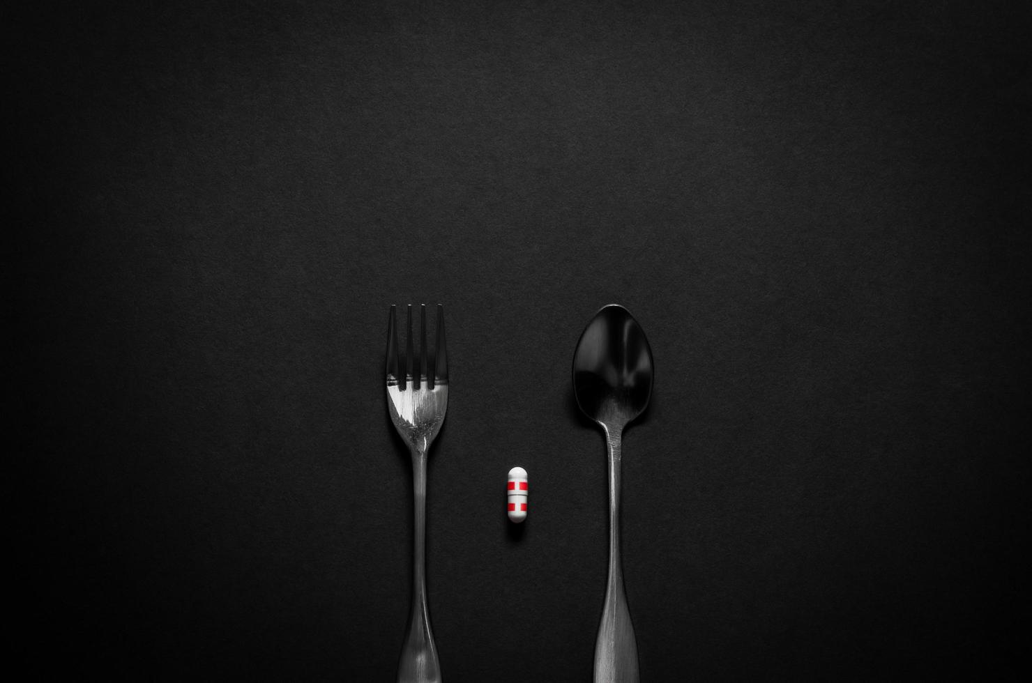Fork and spoon with a capsule medicine on dark background. Minimalist flat lay black for health care concept. photo
