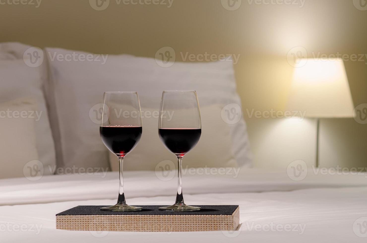 dos copas de vino tinto puestas en la cama en el dormitorio para disfrutar bebiendo con una pareja. foto