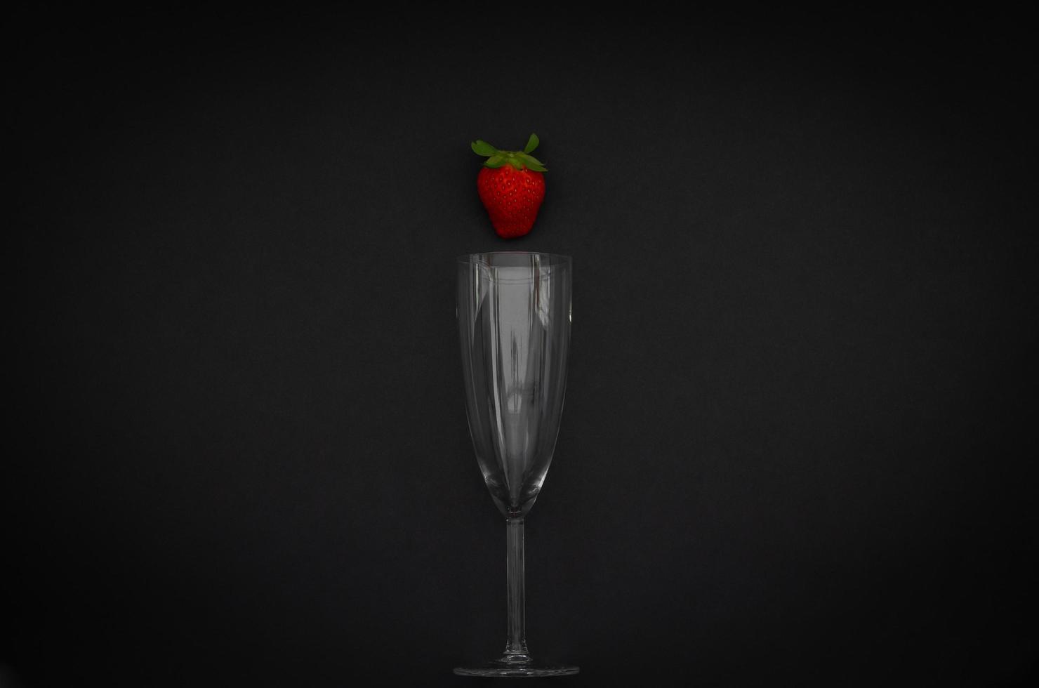 Strawberry and wineglass on dark background for minimalist flat lay black food and drink concept. photo