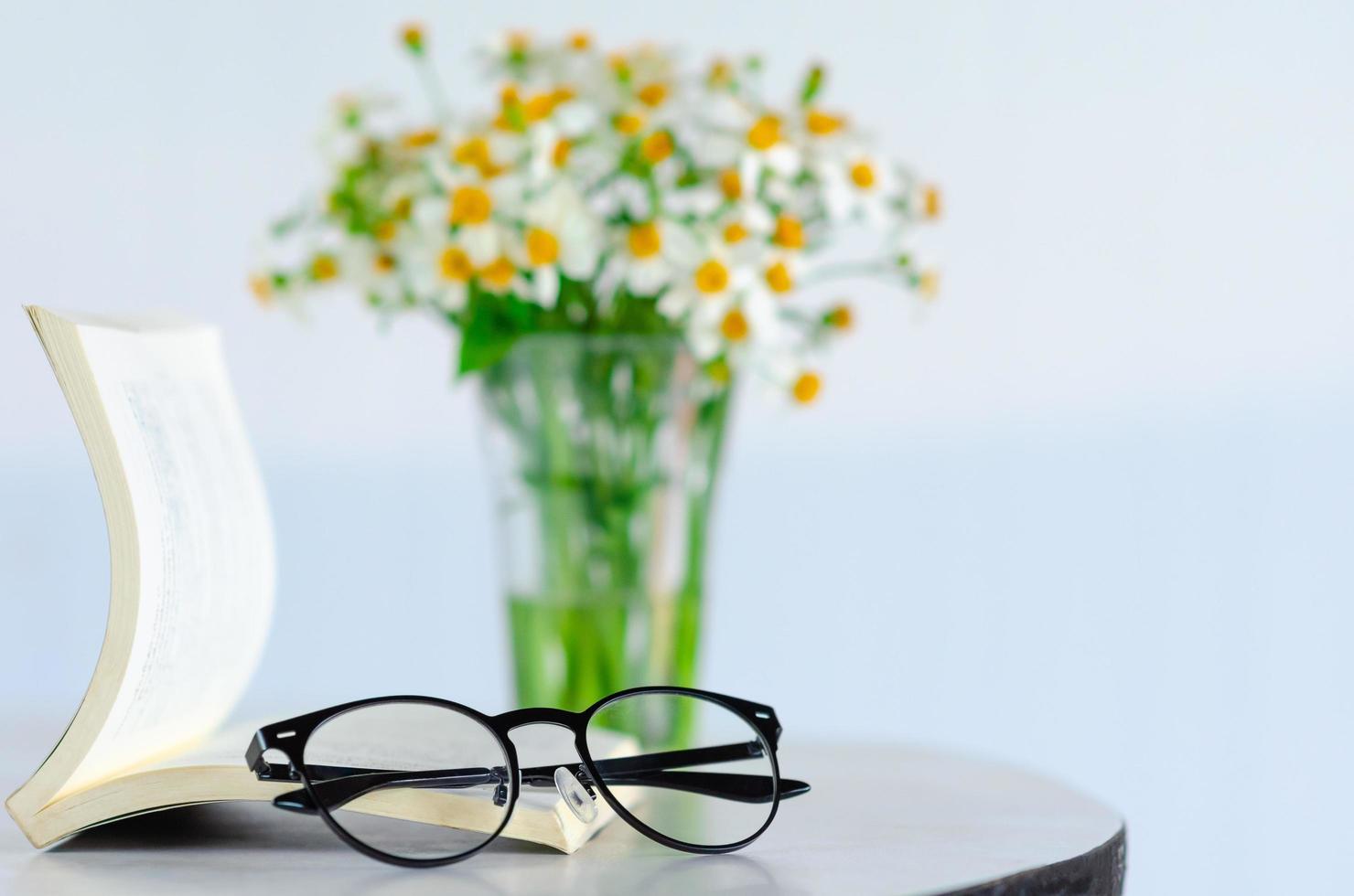 Spectacles puts on a book with blurred flowers background. photo