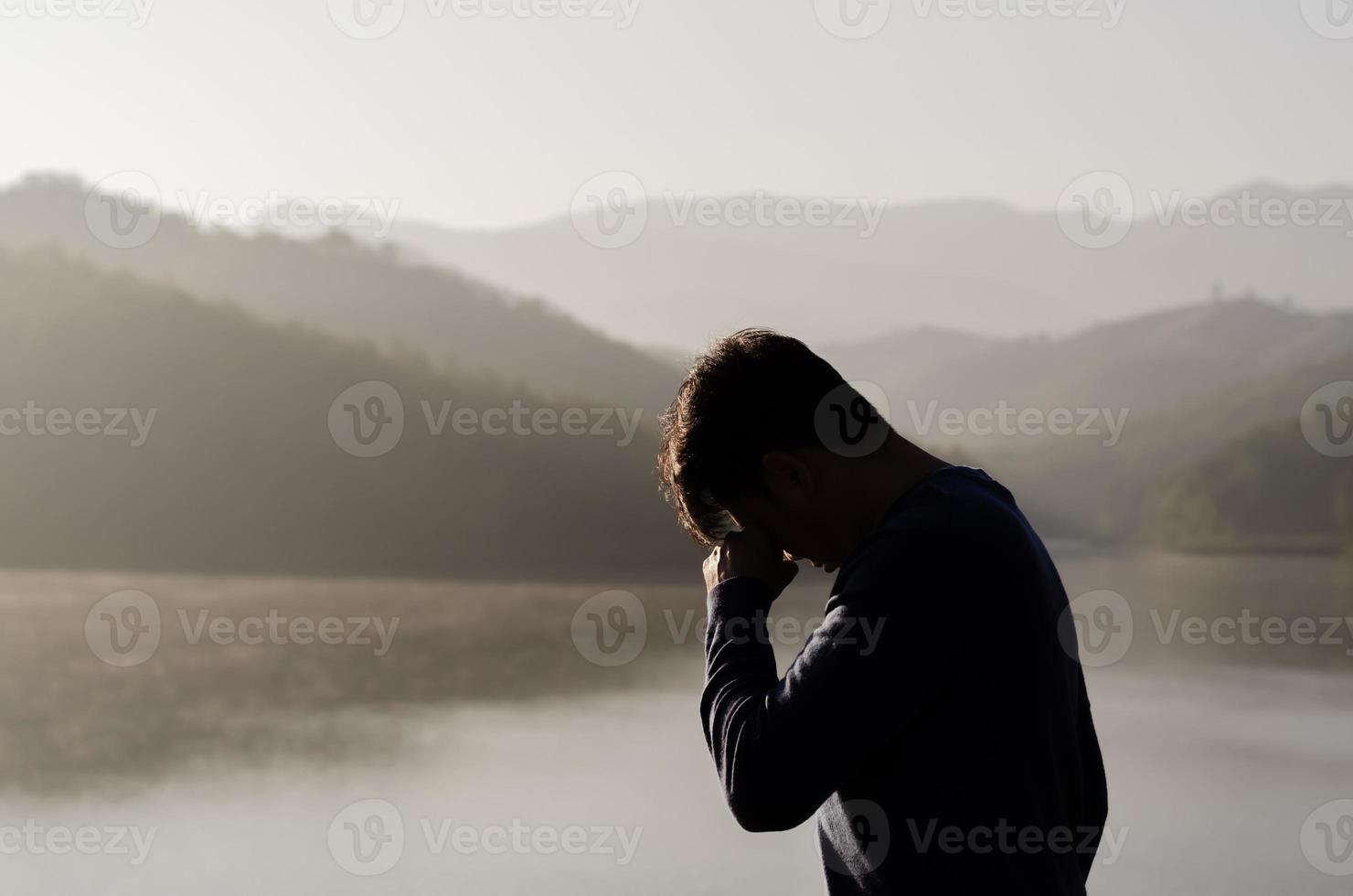 Asian miserable depressed man stand alone with mountain and lake background. Depression and mental health concept. photo