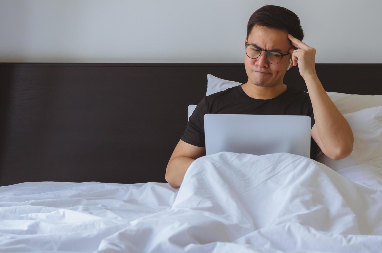 Asian man watching news online at laptop computer and feel confusing in morning on the bed. photo