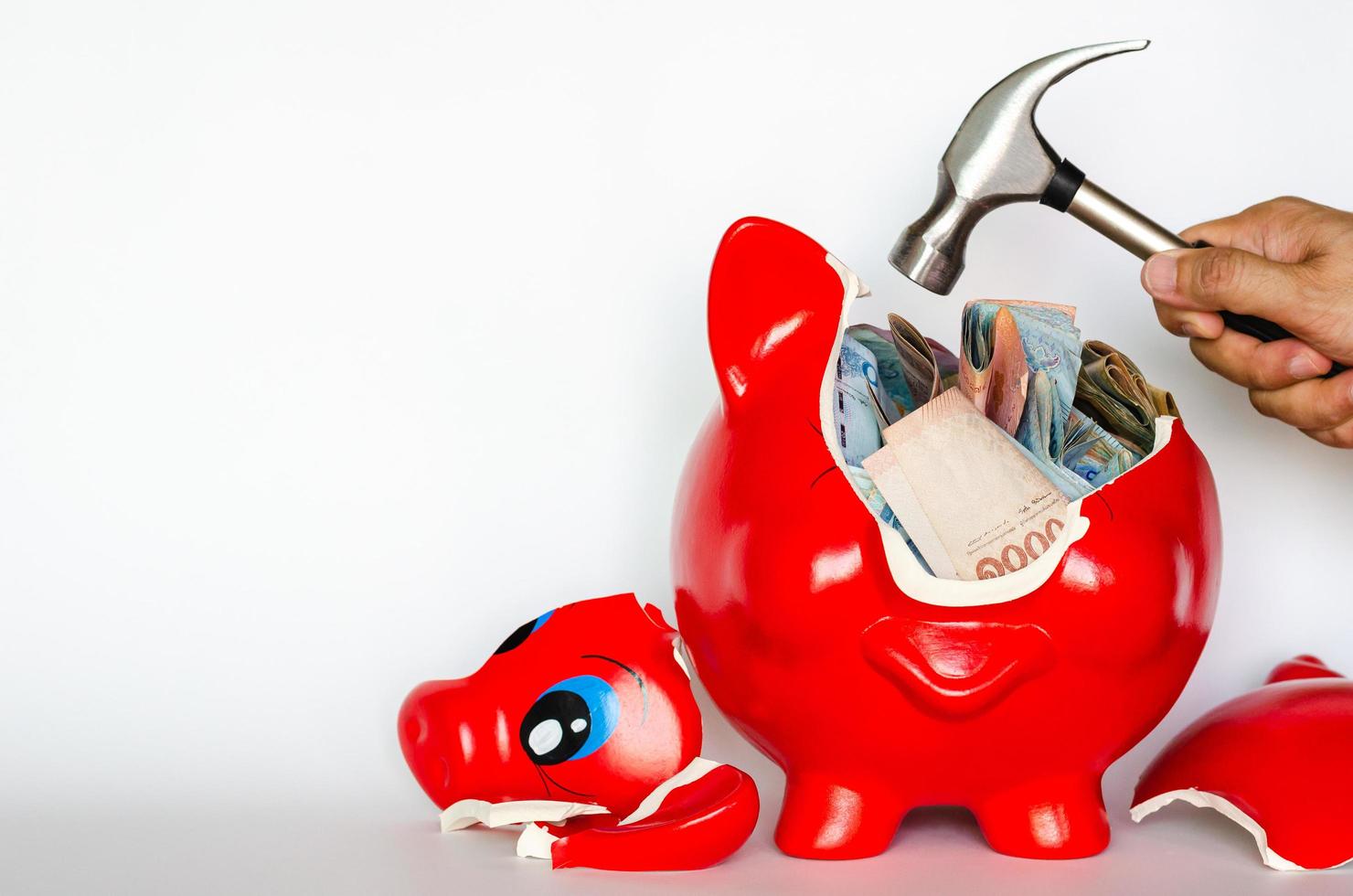 Red piggy bank breaking by the hammer with Thai baht bank note inside put on white background. photo