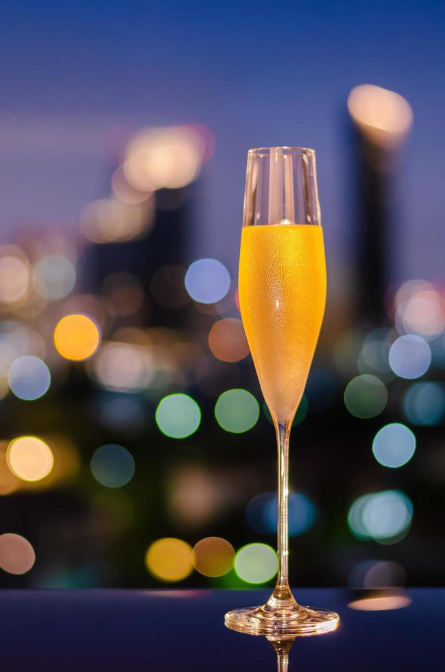 A glass with vapour of cold Champagne on table with colorful city bokeh lights background. photo