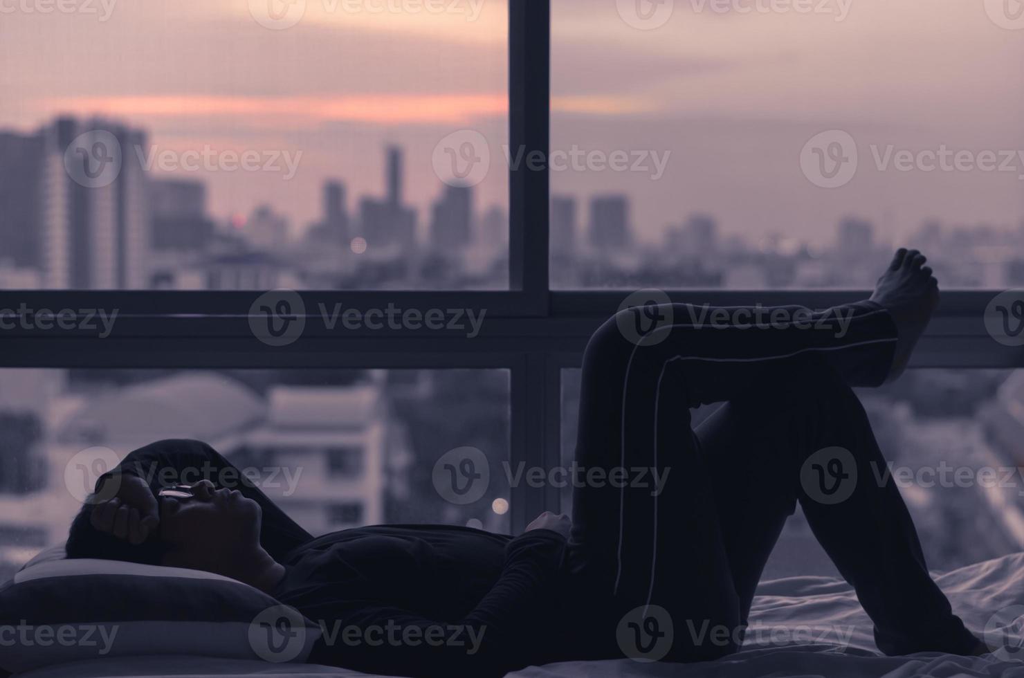 The man lying on bed with city view from bedroom. photo