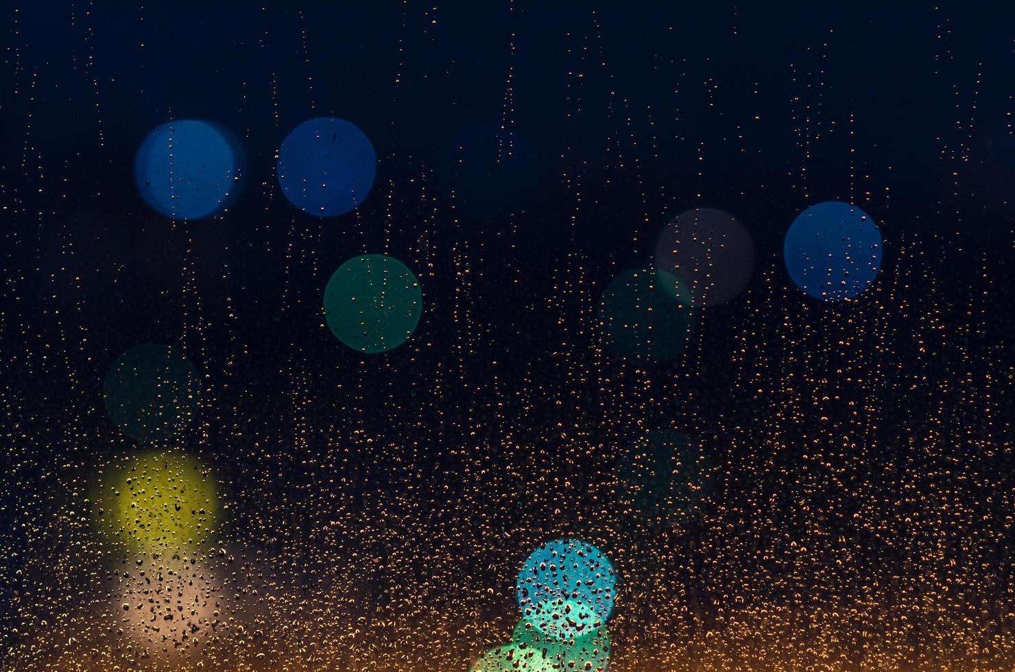 Rain drop on glass window in monsoon season with colorful bokeh lights for abstract and background concept. photo