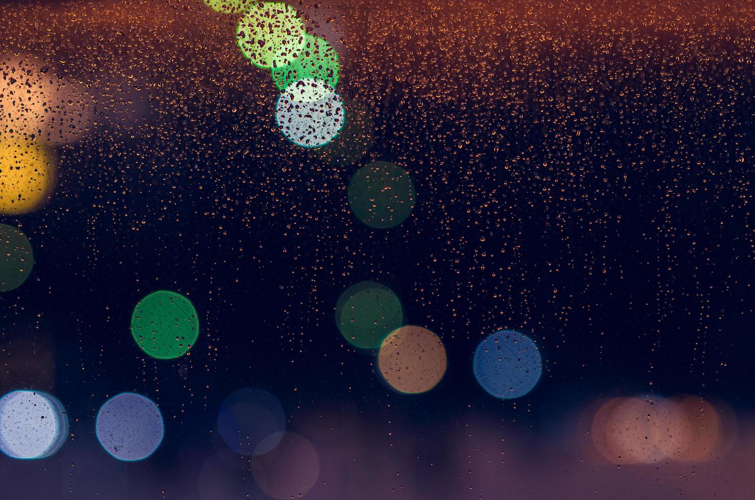 Rain drop on glass window in monsoon season with colorful bokeh lights for abstract and background concept. photo
