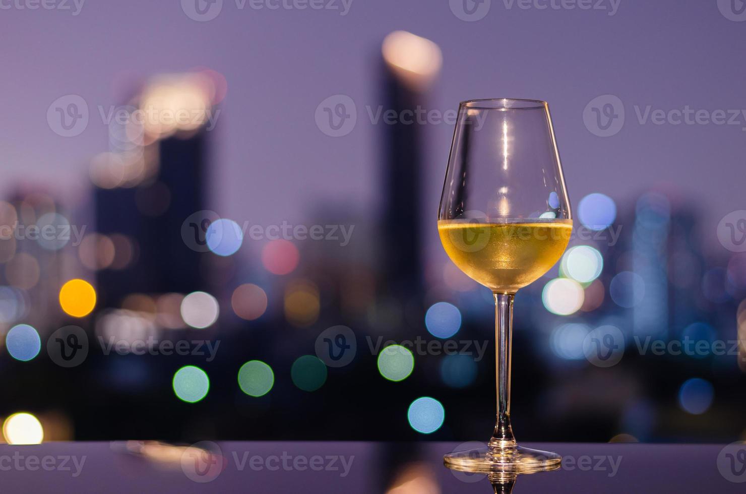 A glass of white wine on table of rooftop bar with colorful city bokeh lights. photo