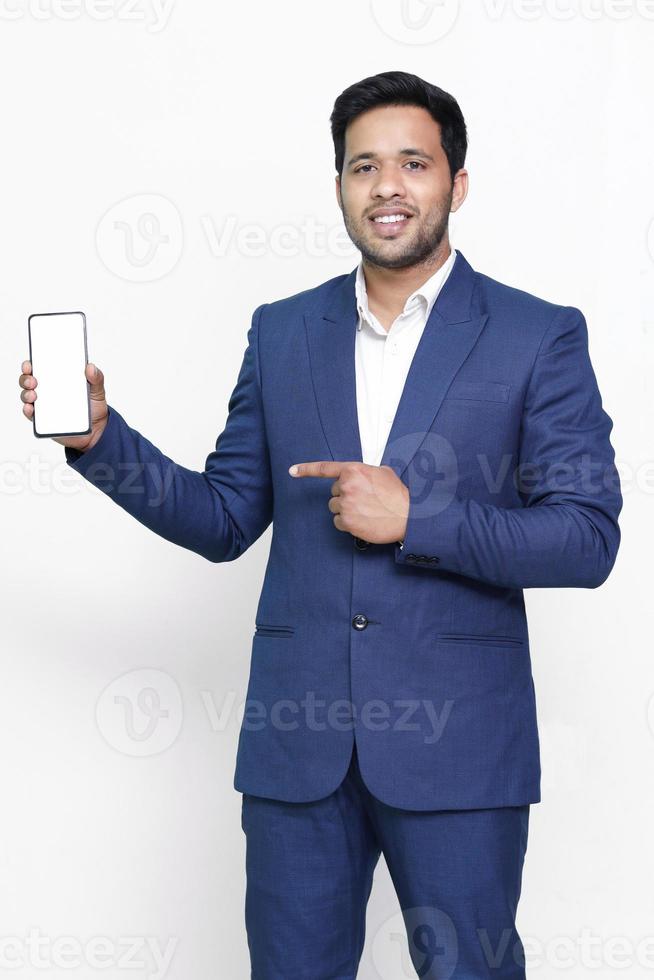 Young businessman in suit, holding blank screen smartphone and pointing to it, copy space for advertising on isolated background. photo