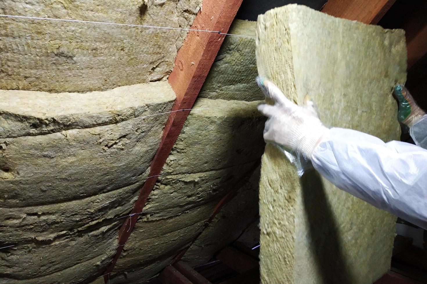 A man in a protective overalls puts mineral wool between the beam of the roof of the house for his warming from the cold photo