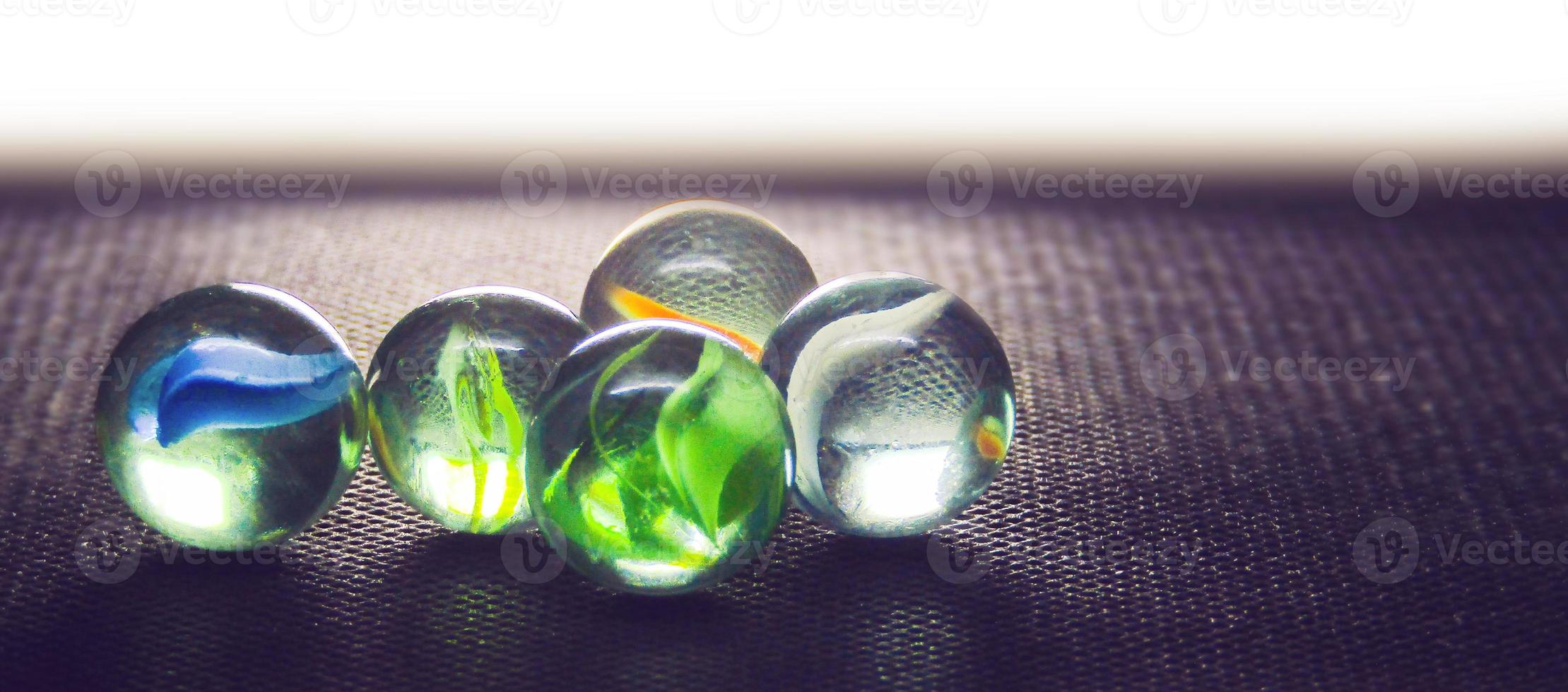Close-up shot of glass marbles on the black table with a backlight. Diversity of marbles color photo