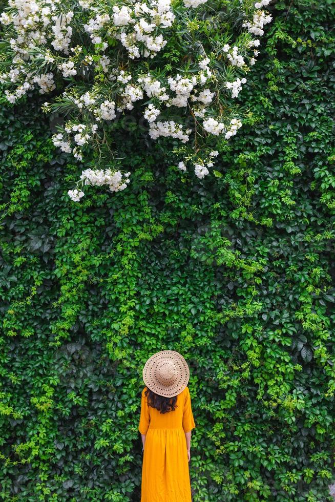 A girl in a straw hat stands near a wall overgrown with ivy photo