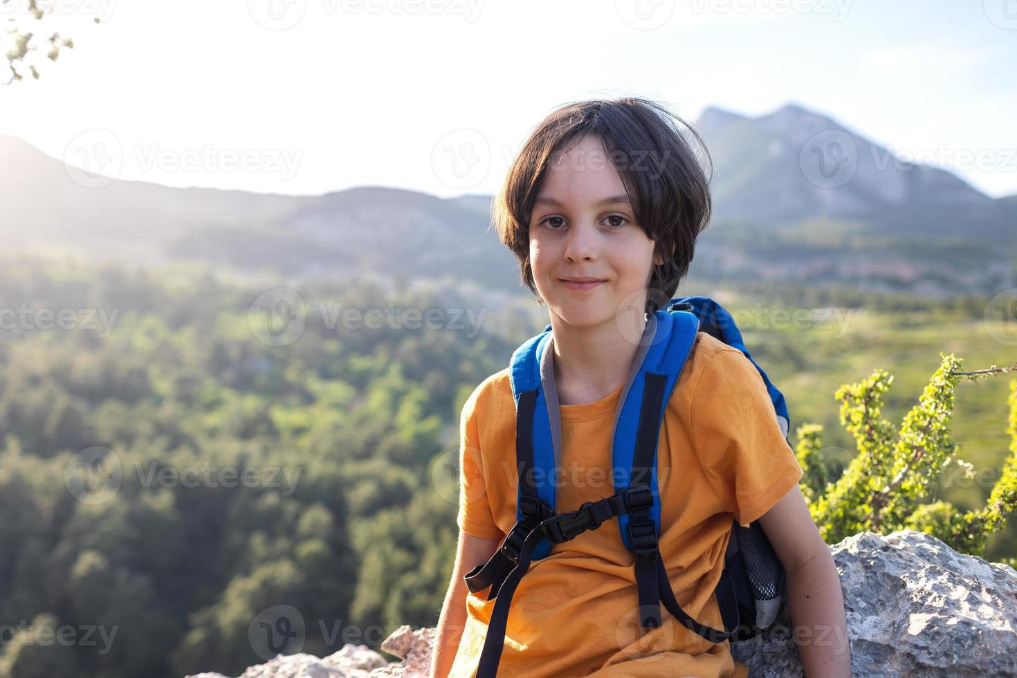 un niño con una mochila se para en la cima de una montaña foto