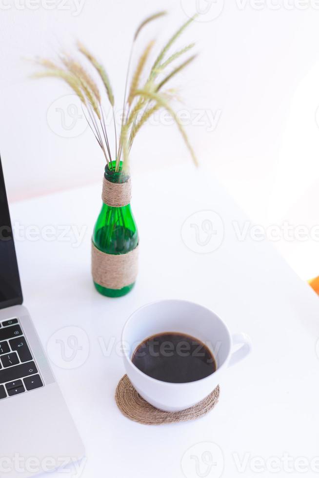 lugar de trabajo independiente, computadora portátil, taza de café y planta en maceta en la mesa blanca foto