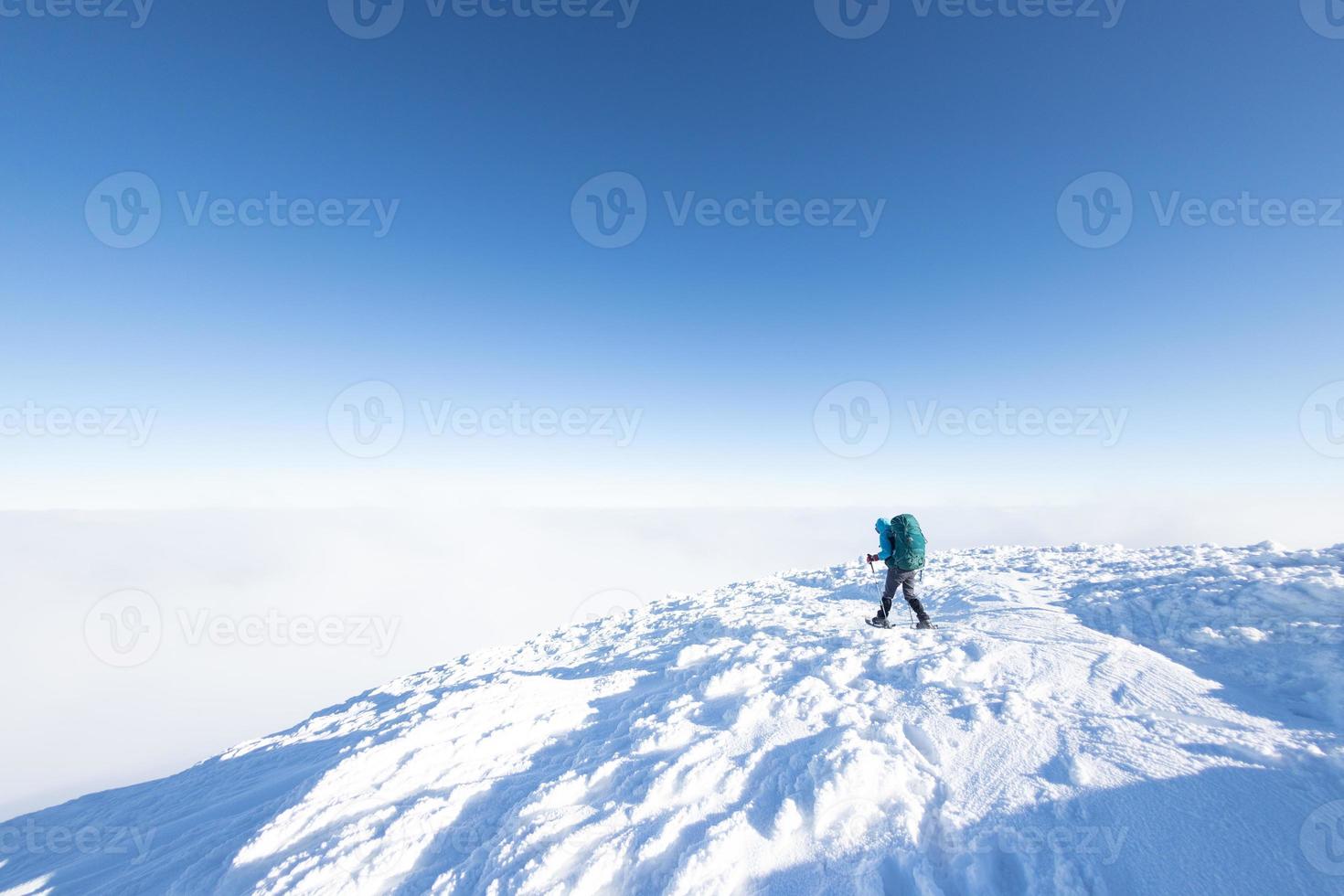 A woman with a backpack in snowshoes climbs a snowy mountain photo