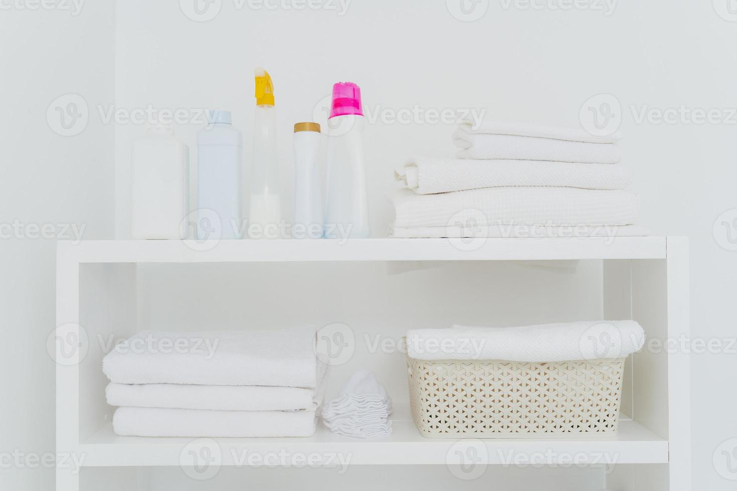 Laundry room with neatly folded towels, bottles of liquid washing or detergents. Everything in white colors. Daily chores and laundry day photo