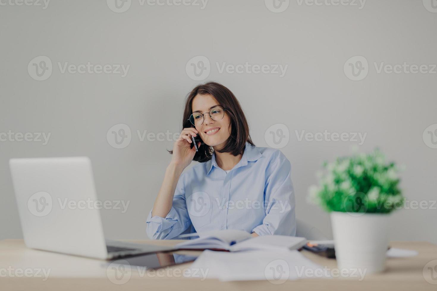 Beautiful female recruiter makes job offer to somene via cell phone, checks curriculum vitae on laptop computer, expalins detailes and pluses of work, surrounded with flower and personal diary photo