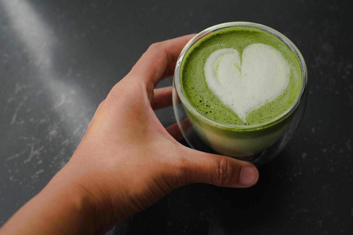 Top view of hand hold a cup of hot matcha green tea latte art in double walled glass on table in the cafe. Flat lay. photo