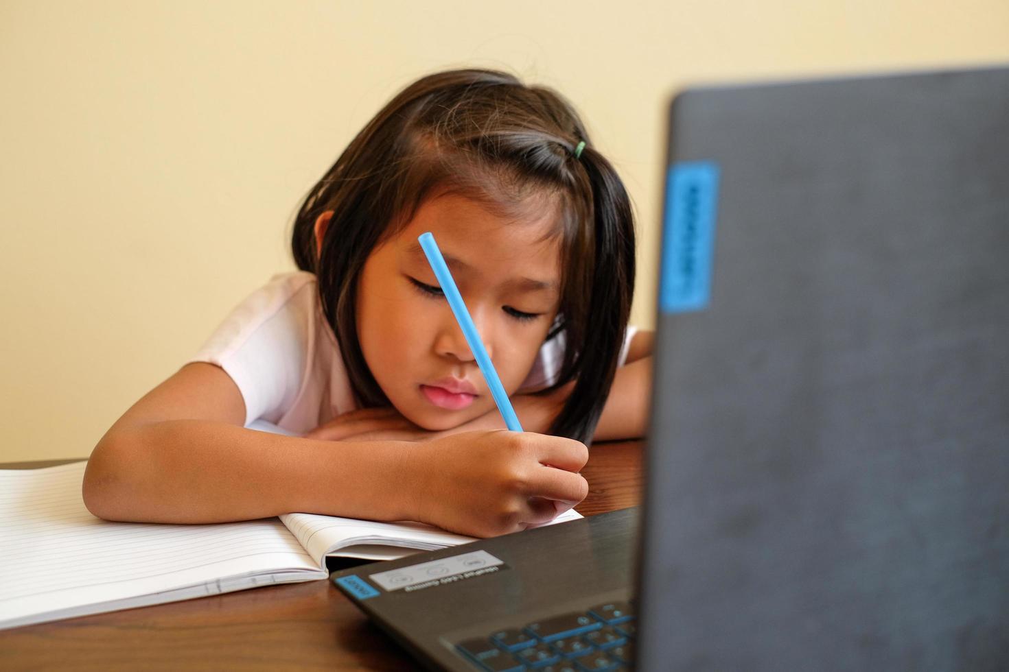 niña tailandesa en clase de aprendizaje en línea en casa durante la situación del covid-19. cuaderno de aprendizaje del estudiante durante la cuarentena. sentirse aburrido. foco seleccionado. educación en línea, concepto de escuela en casa. foto