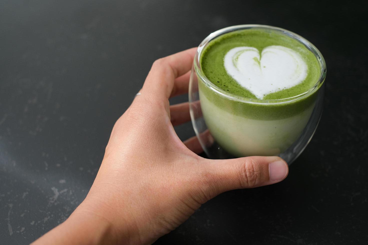 Top view of hand hold a cup of hot matcha green tea latte art in double walled glass on table in the cafe. Flat lay. photo