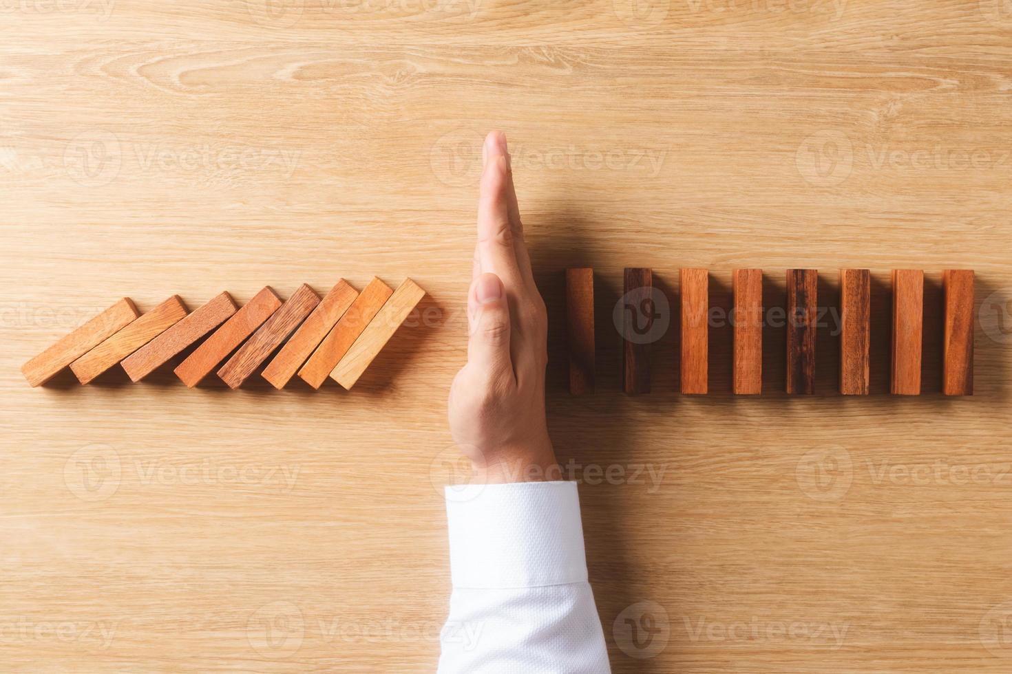 Risk management and business strategy concept, businessman hands stop the dominoes from falling continuously, preventing future risks from crisis. photo