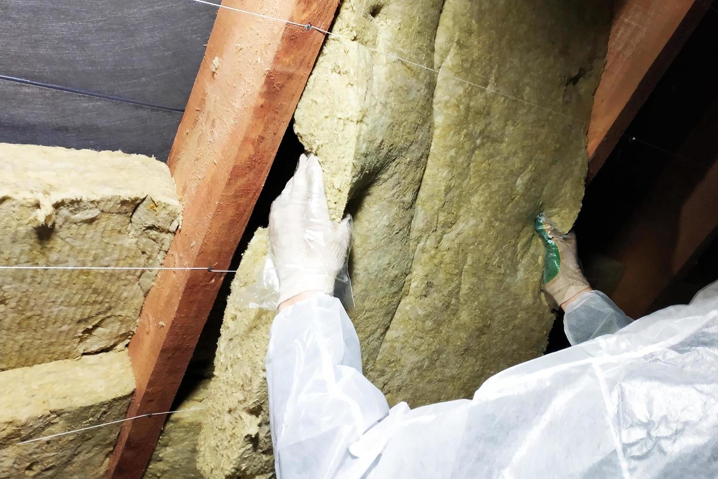 A man in a protective overalls puts mineral wool between the beam of the roof of the house for his warming from the cold photo