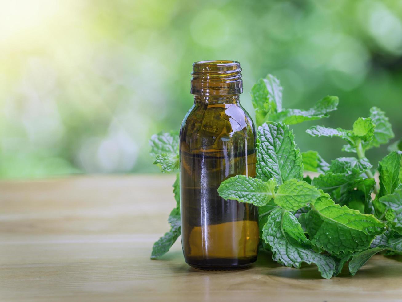 The peppermint extract in small bottle near peppermint leaf on wooden table. The essential oil falling from glass dropper into organic bio alternative medicine, brown bottle. photo