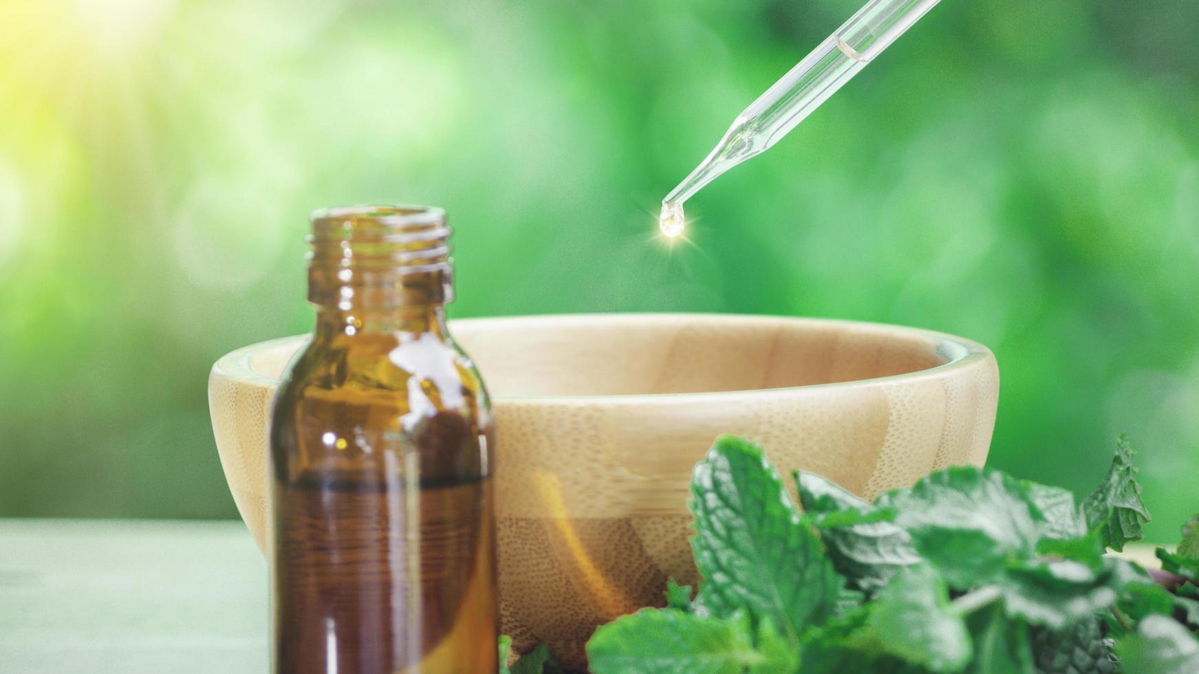 The peppermint extract in small bottle near peppermint leaf on wooden table. The essential oil falling from glass dropper into organic bio alternative medicine, brown bottle. photo