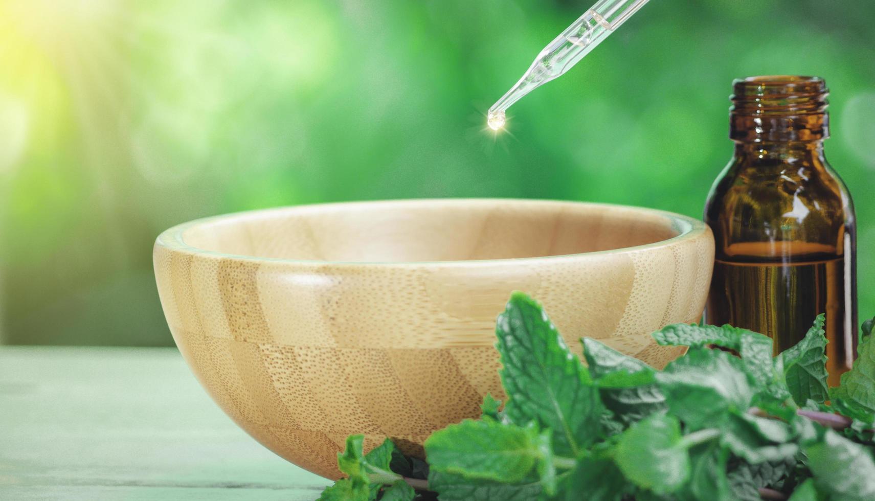 el extracto de menta en una botella pequeña cerca de la hoja de menta sobre una mesa de madera. el aceite esencial que cae del gotero de vidrio a la medicina bio alternativa orgánica, botella marrón. foto