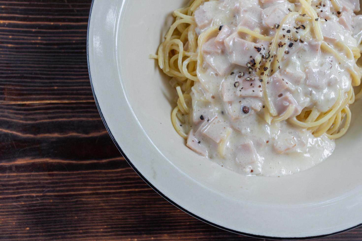 spaghetti carbonara, a delicious mix of ham, bacon and hot cheese, served in a white plate on a ready to eat wooden table. Delicious spaghetti with carbonara sauce mixed with ham, bacon and cheese. photo