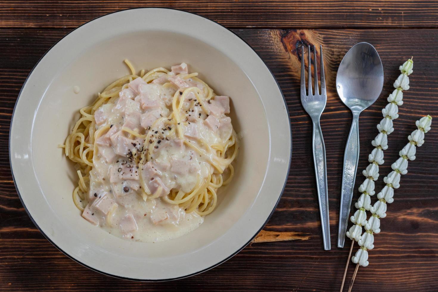 spaghetti carbonara, a delicious mix of ham, bacon and hot cheese, served in a white plate on a ready to eat wooden table. Delicious spaghetti with carbonara sauce mixed with ham, bacon and cheese. photo
