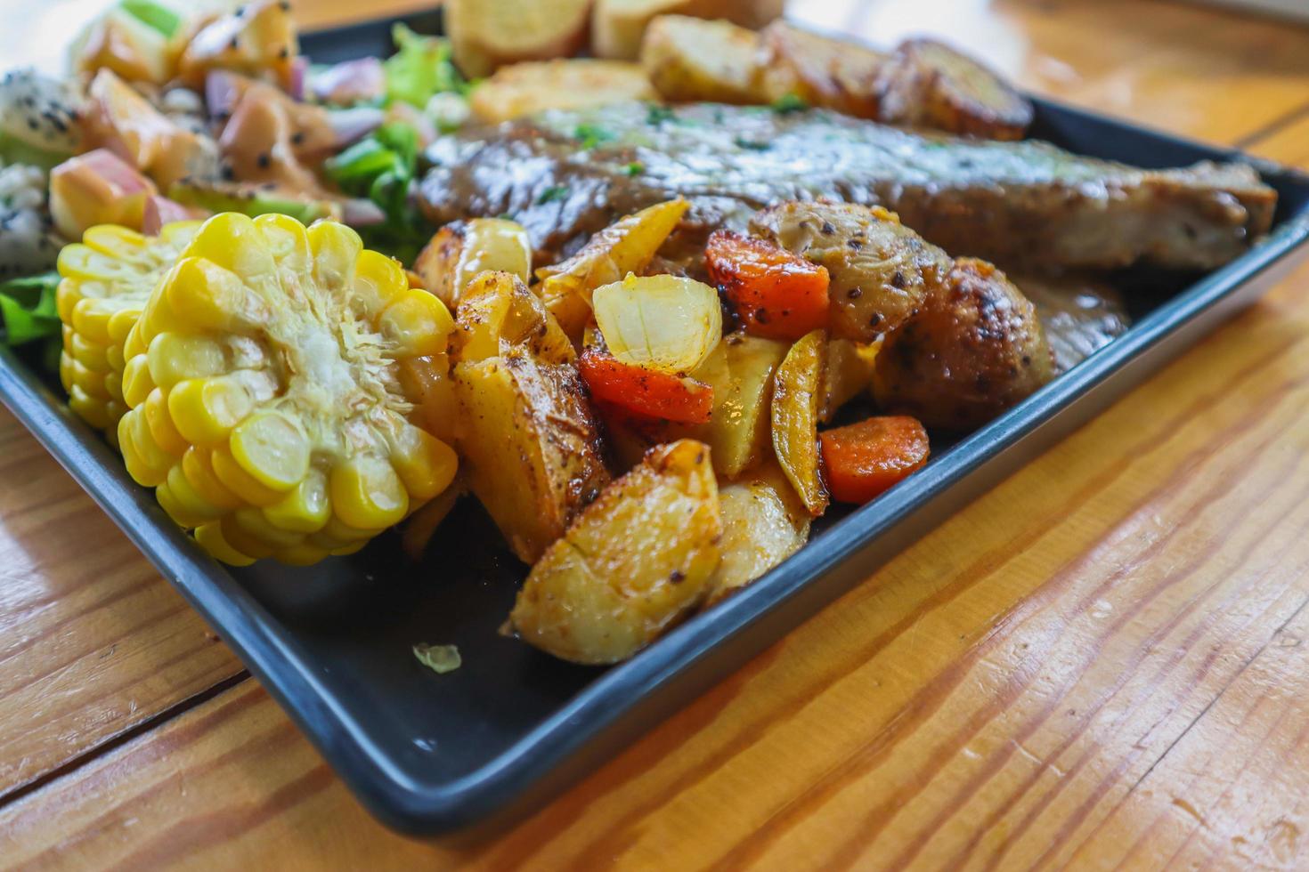 Grilled beef steak with gravy is served with a fruit and vegetable salad inside a black ceramic plate on the dining room table to prepare the steak for a festive dinner. photo