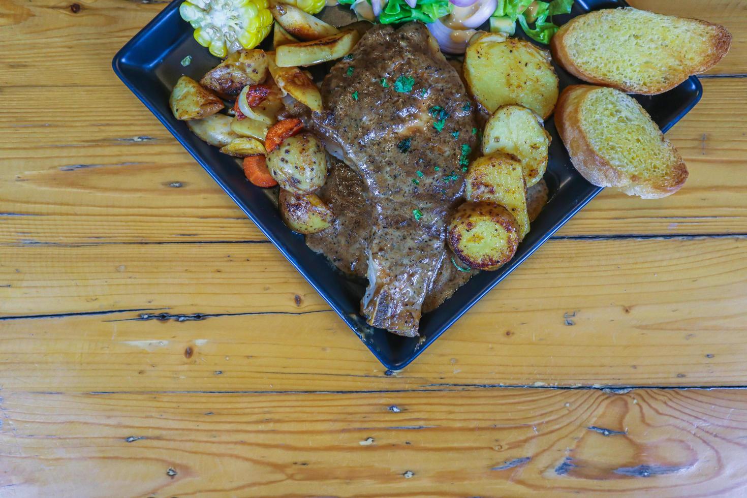 Grilled beef steak with gravy is served with a fruit and vegetable salad inside a black ceramic plate on the dining room table to prepare the steak for a festive dinner. photo