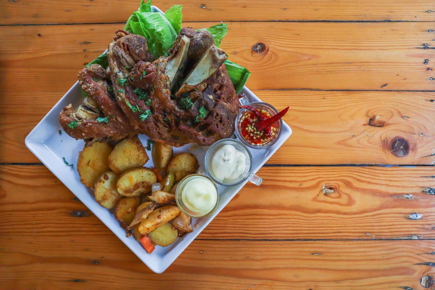 German pork knuckle is served with baked potatoes and sauce inside a white ceramic plate placed on the dining room table to make the pork knuckle ready for a dinner feast. photo