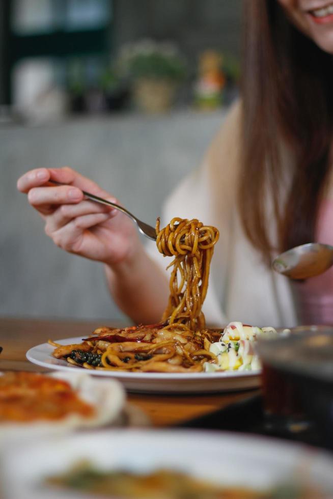 Asian woman eating spaghetti with spicy seafood sauce in a restaurant. The spicy seafood spaghetti was served in a plate and placed on the dining table as the woman ordered. photo