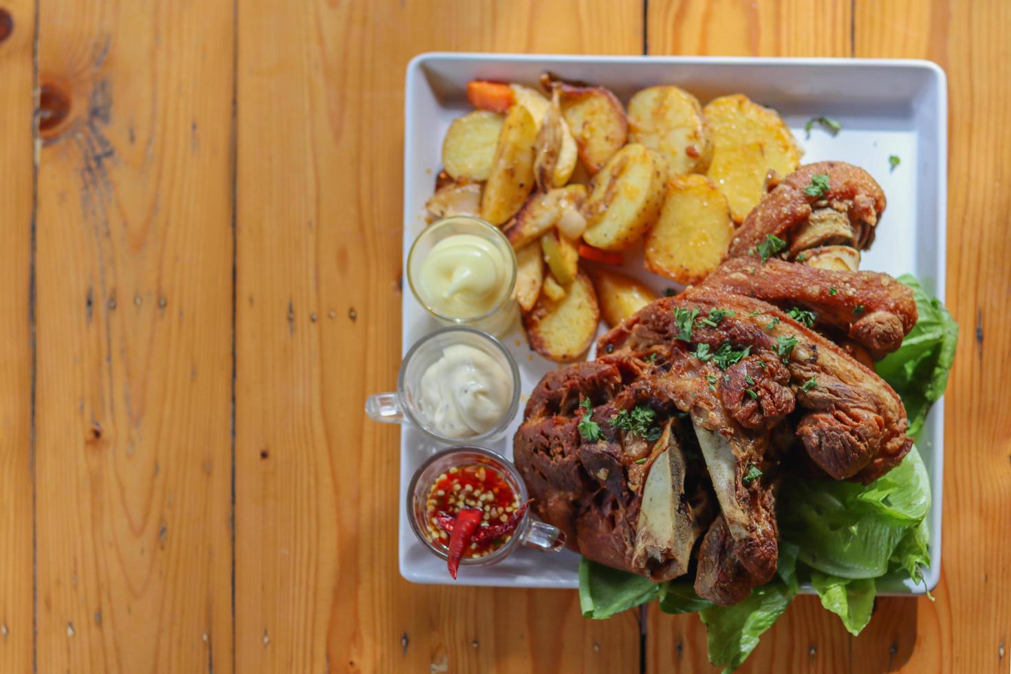 German pork knuckle is served with baked potatoes and sauce inside a white ceramic plate placed on the dining room table to make the pork knuckle ready for a dinner feast. photo